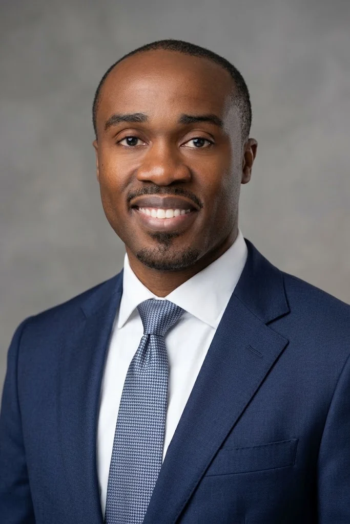 Mo Yusuf headshot, navy suit, grey background